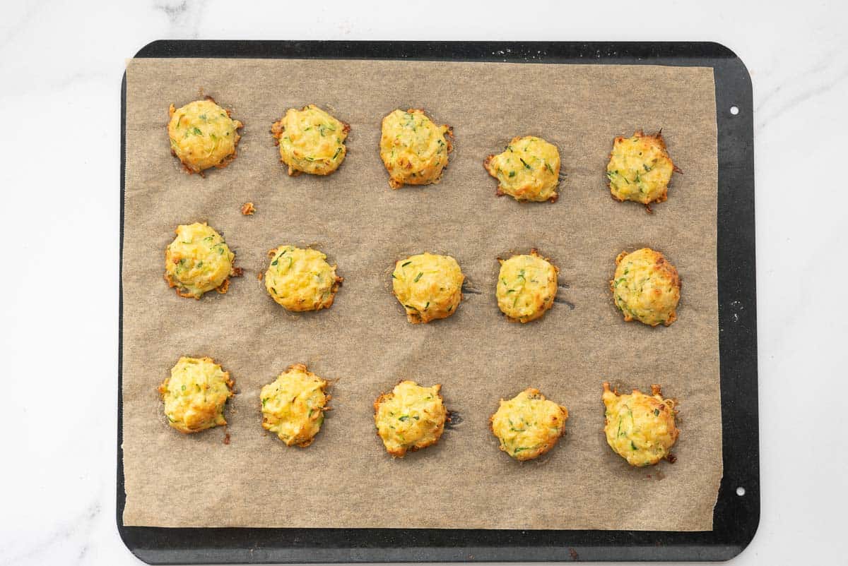 15 golden baked zucchini tots on a lined baking tray.