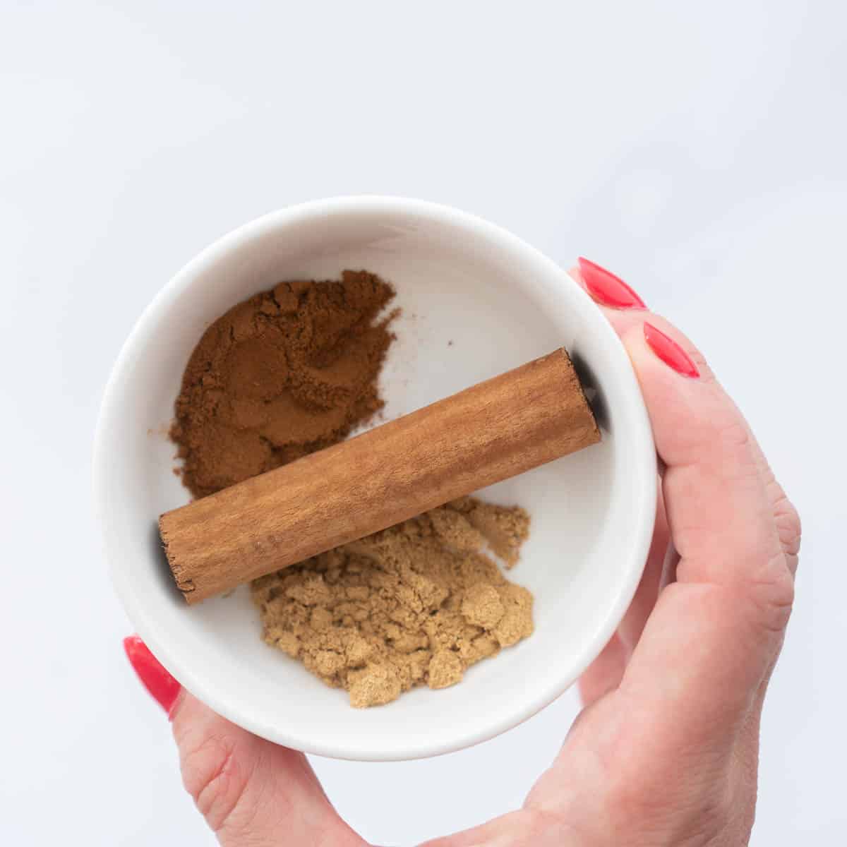 A small ceramic bowl containing ground nutmeg, ginger and a cinnamon stick.