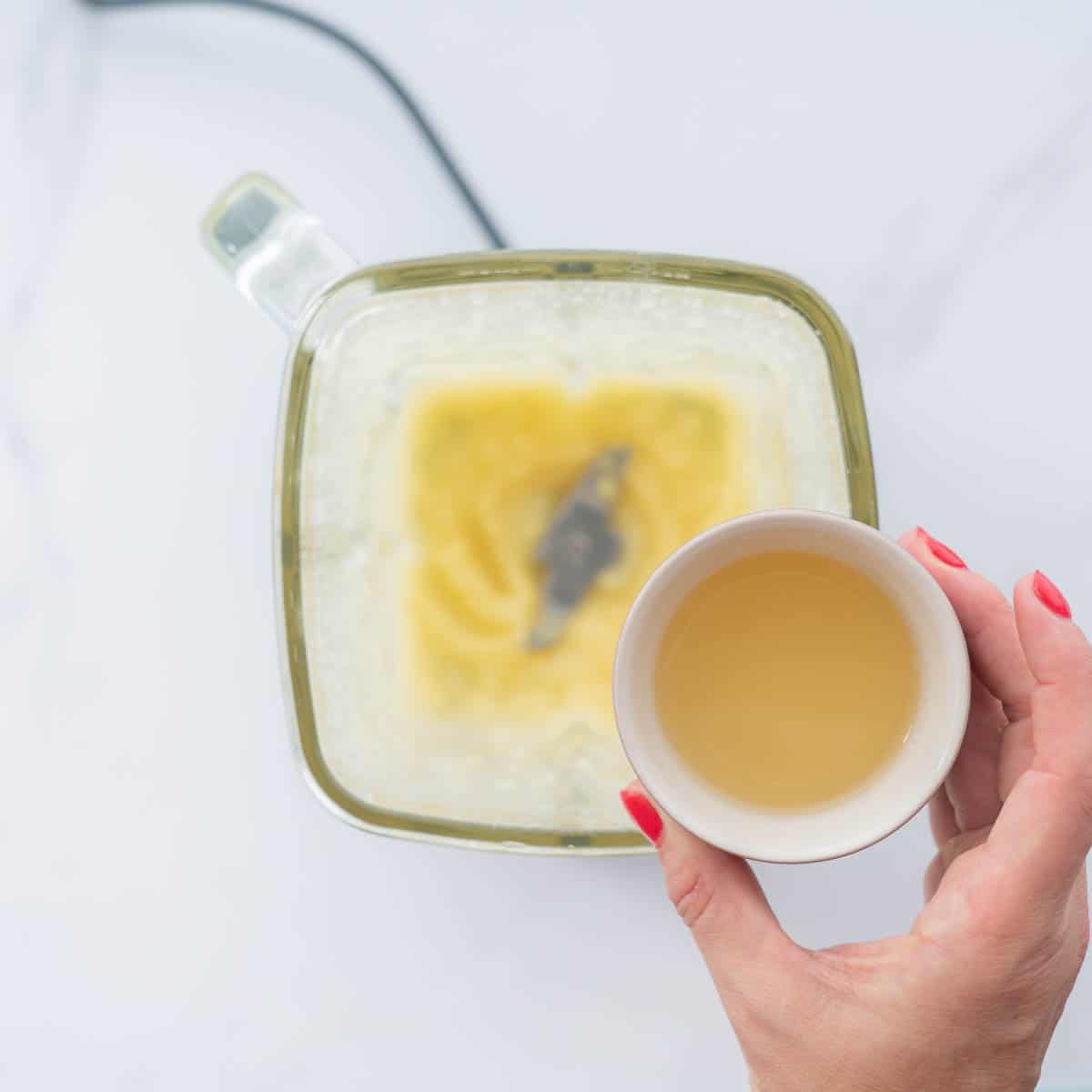 A small bowl of reserved apple liquid being held above a blender of pureed apple.