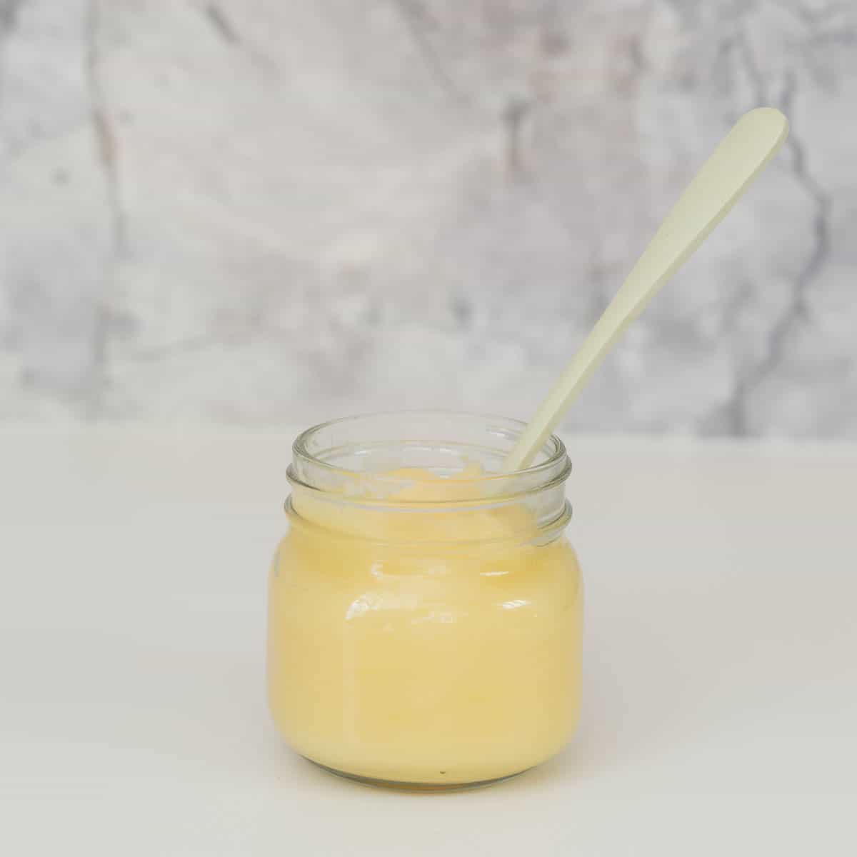 A small glass jar of apple puree with a green bamboo spoon in front of a marble splash back. 