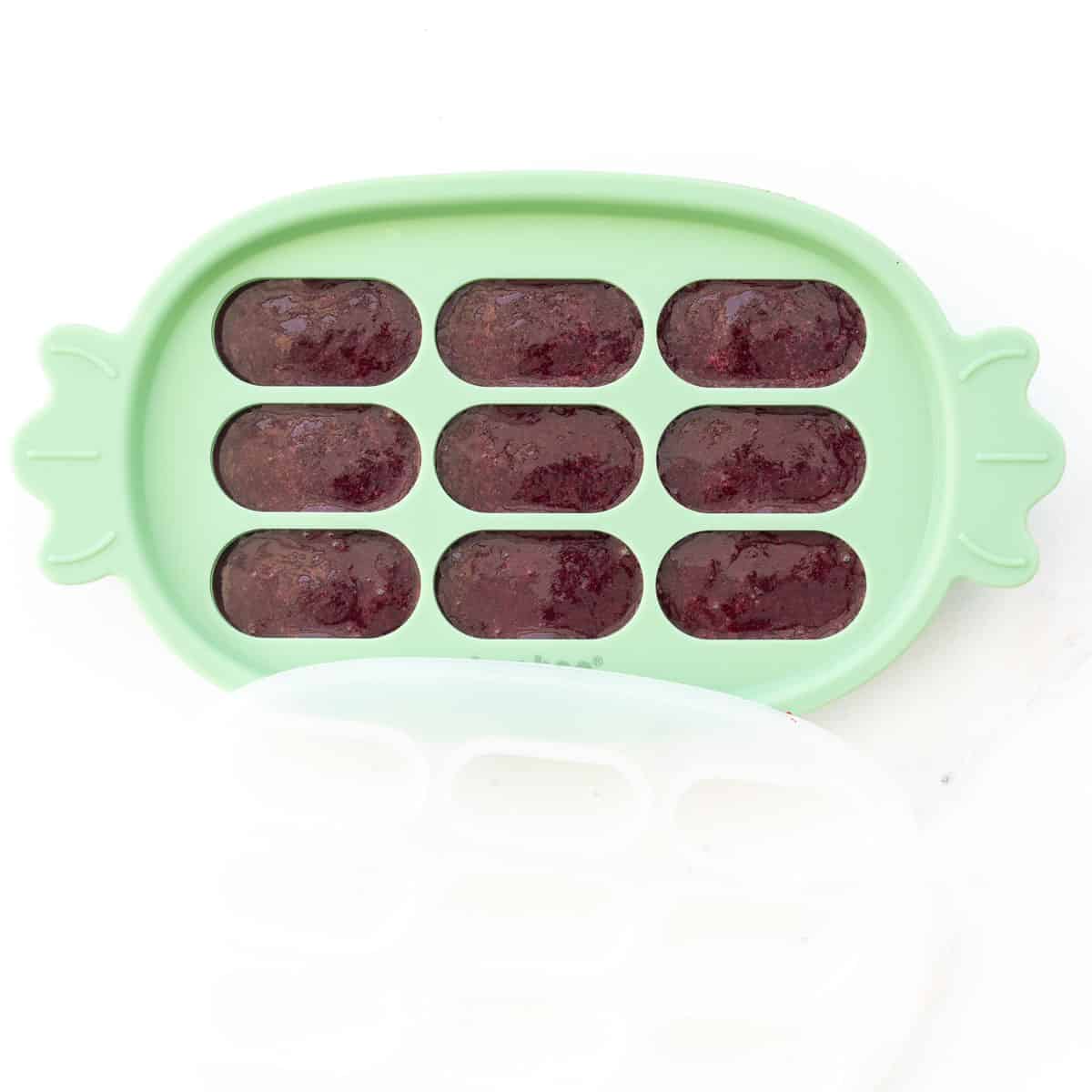 Purple baby food in a green silicone ice cube tray. 