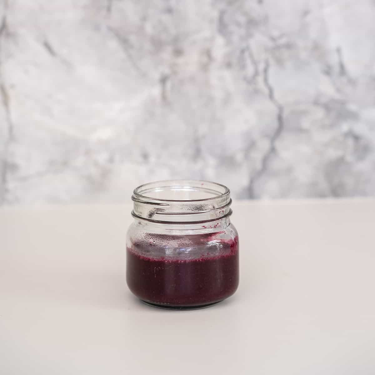 Purple blueberry puree in a small glass jar in front of a marble splash back.