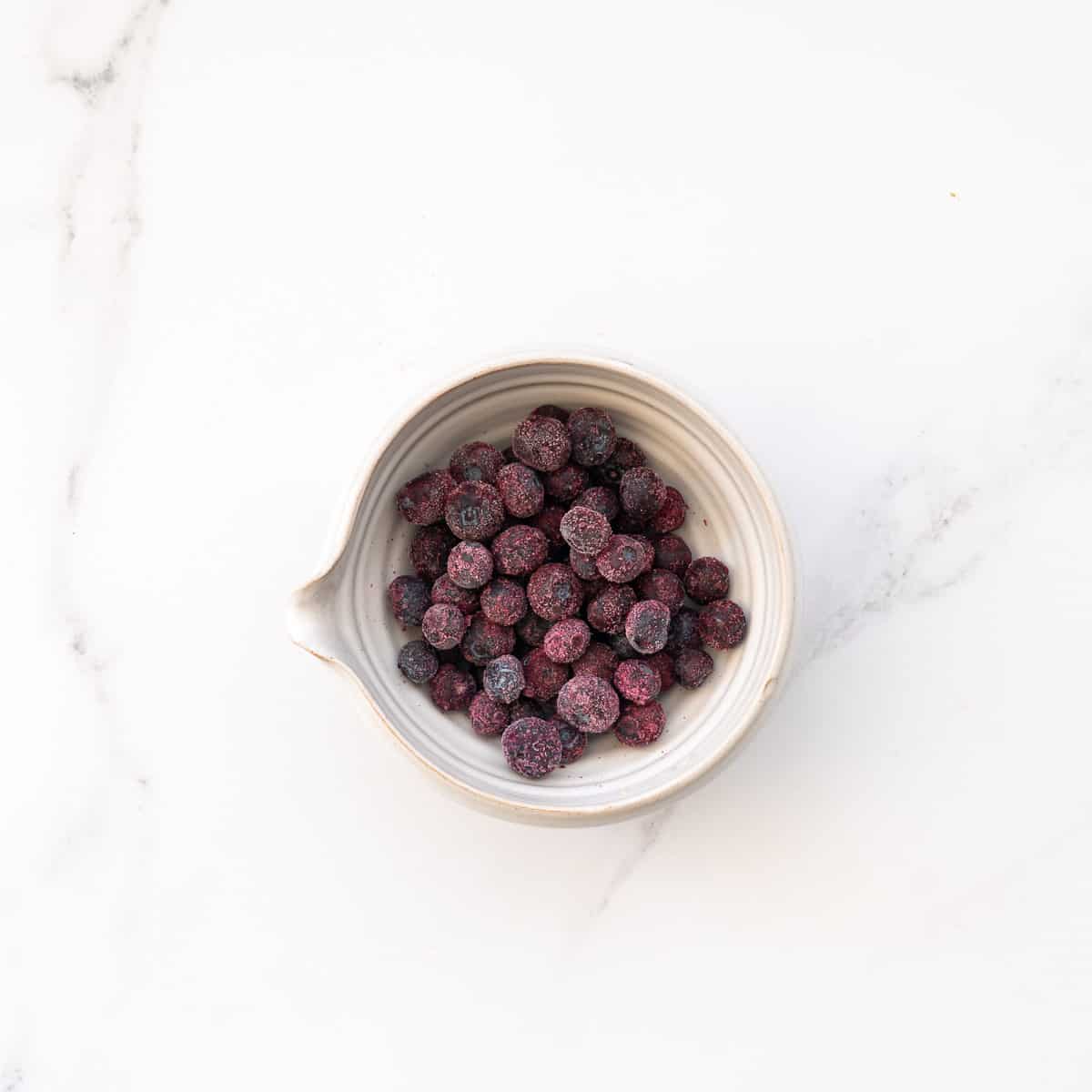 A white ceramic bowl of frozen blueberries.