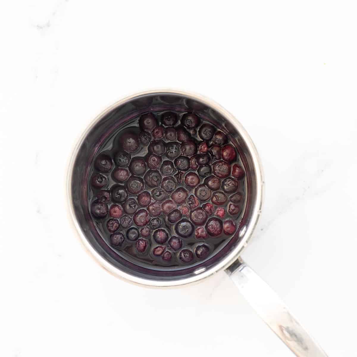 Frozen blueberries and water in a small stainless steel saucepan.
