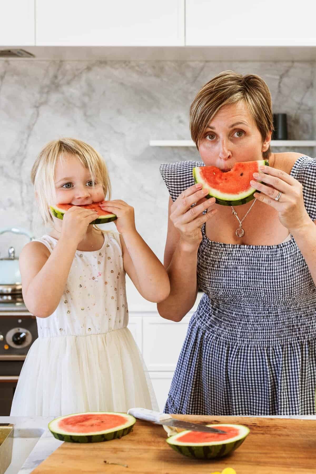 A mother and a toddler both biting into large slices of watermelon.
