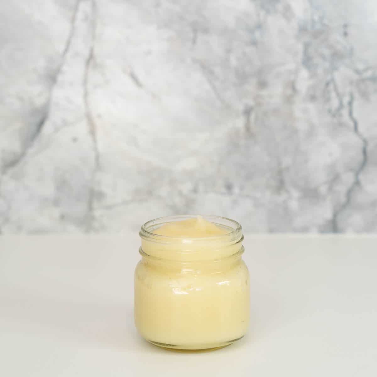 A glass jar of pear puree on a bench.