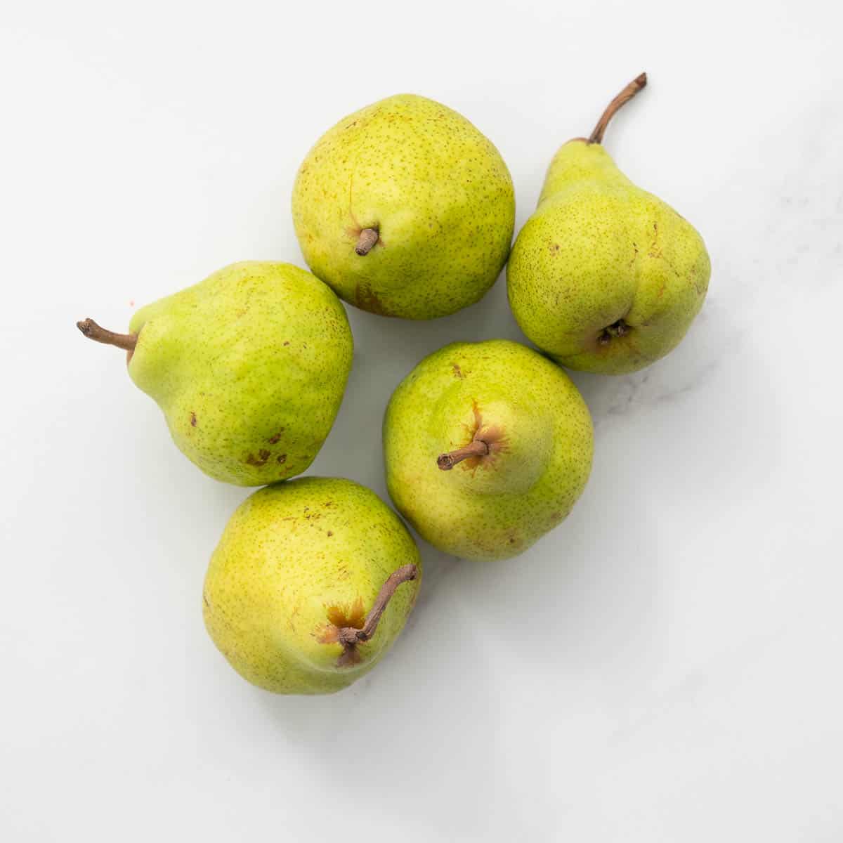 5 green pears on a white marble bench top.