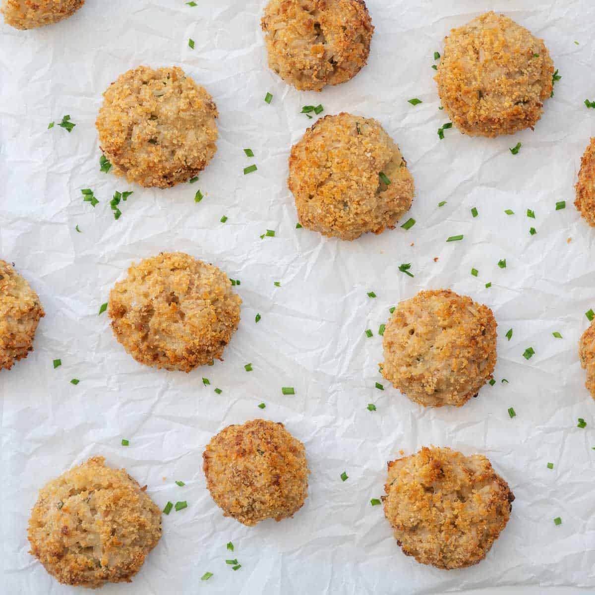 Goldem brown tuna rice balls on crinkled parchment paper scattered with chopped chives.