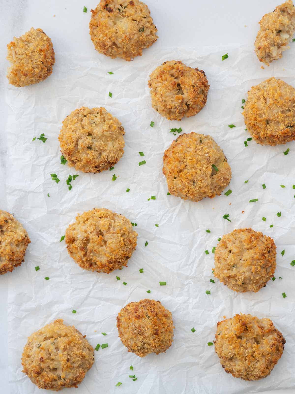 Golden brown tuna rice balls on crinkeled parchment paper scattered with chopped chives.