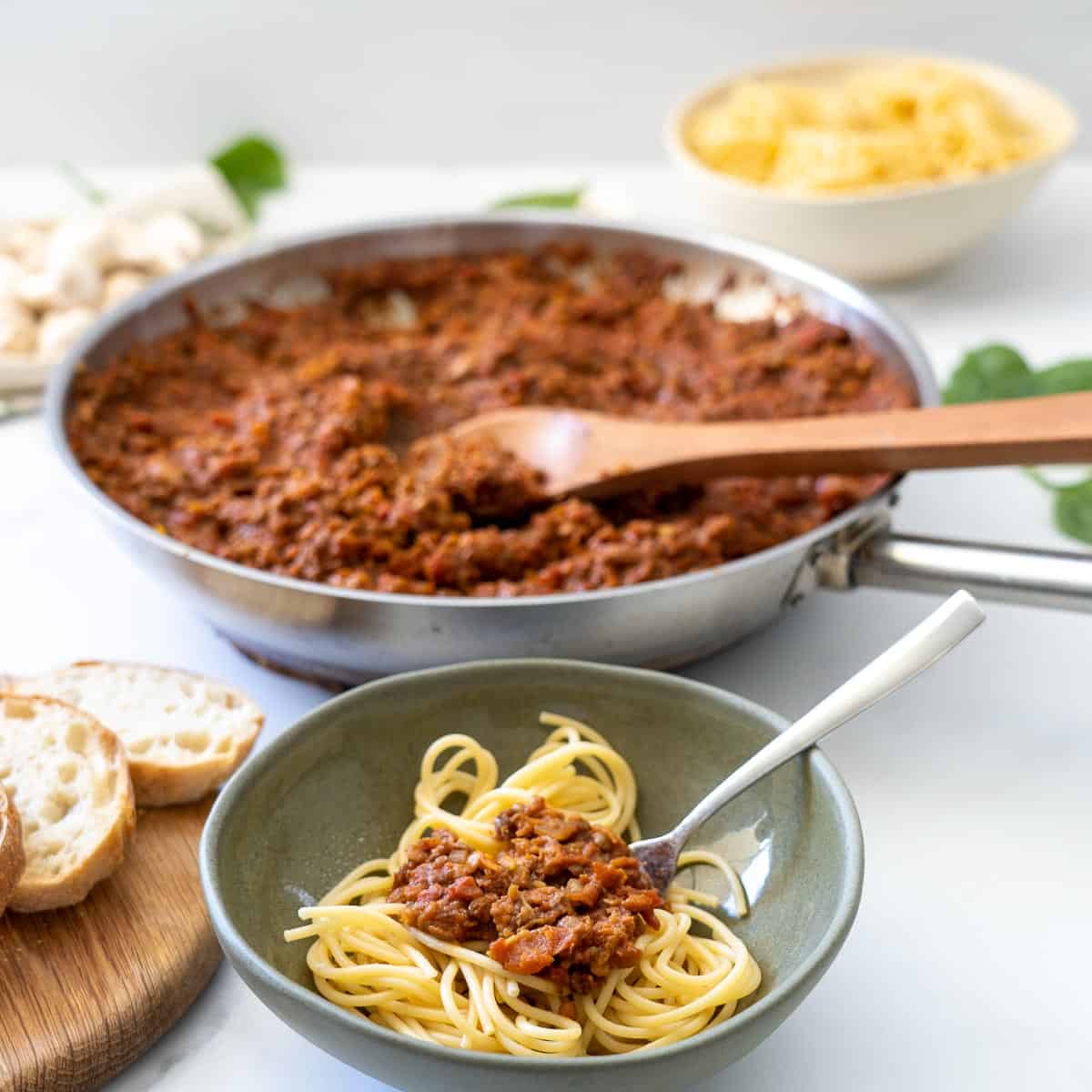 A bolw of spaghetti bolognese sitting on a table next to a large fry pan of bolognese sauce, 