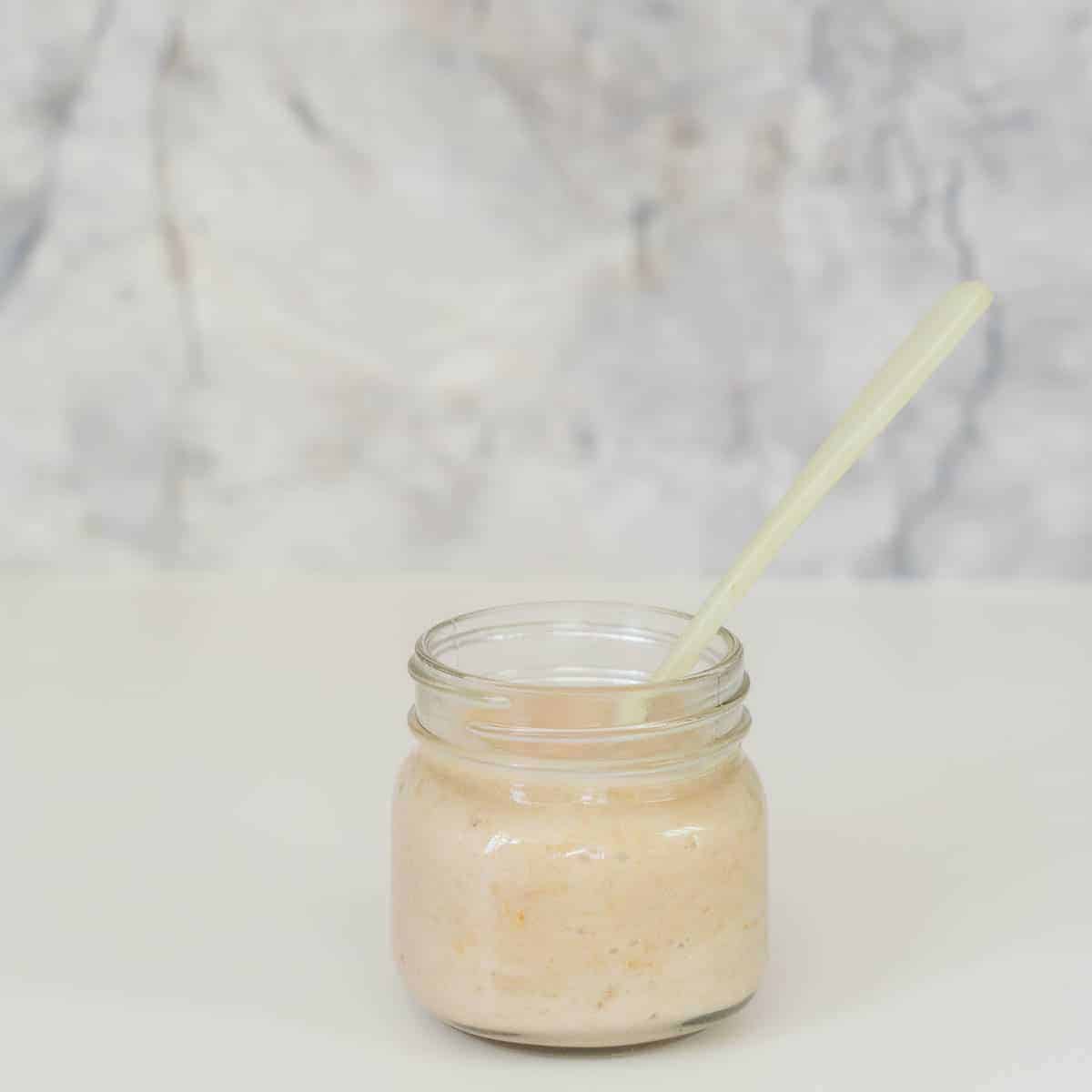 A jar of creamy coloured puree with a spoon in tit
