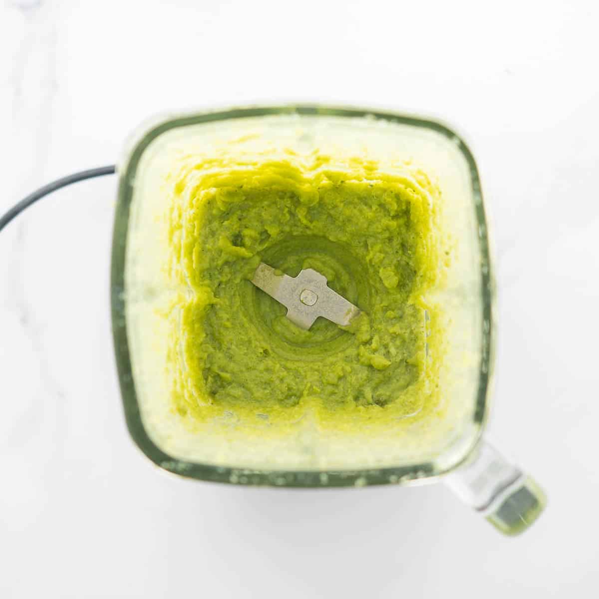 Green pureed broccoli in a glass blender jug.