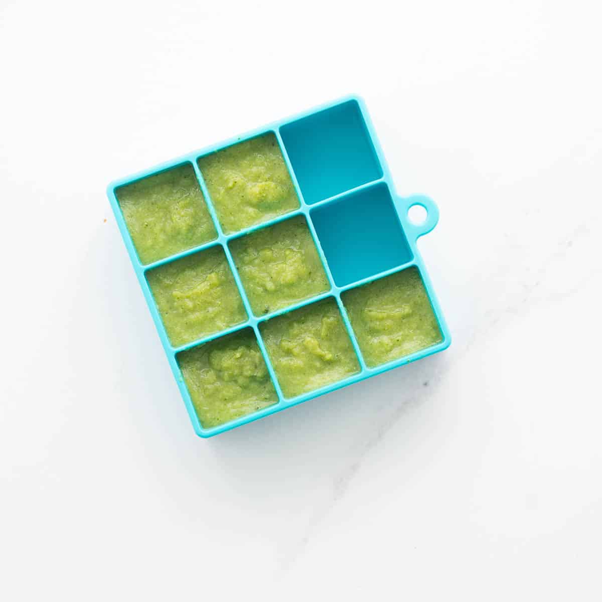 Broccoli puree in a blue silicone ice cube tray ready to be frozen.