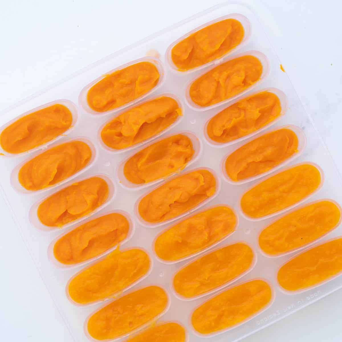 An ice tray filled with orange puree ready to freeze