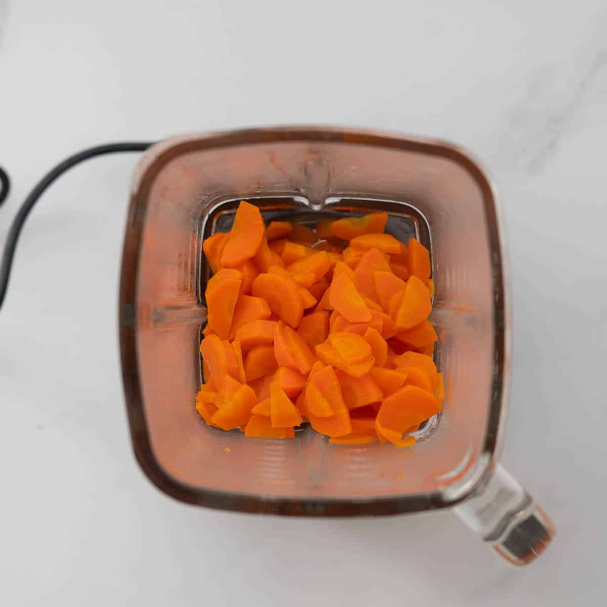 Tender cooked carrot slices in a glass blender jug.