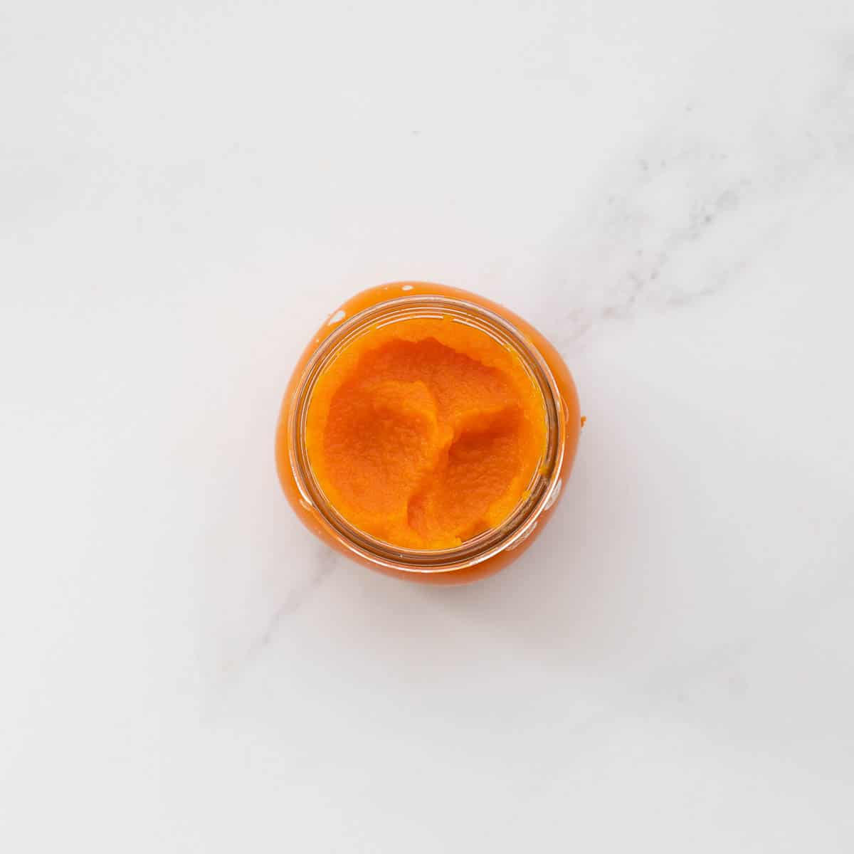 A small glass jar filled with vibrant orange vegetable puree. 