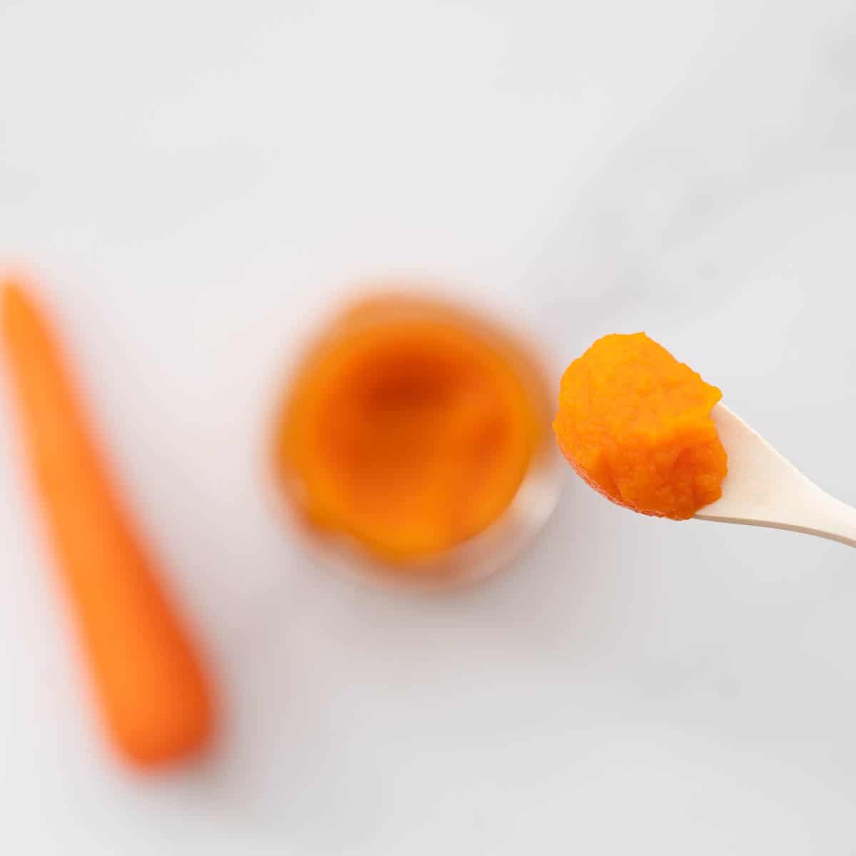A spoonful of carrot puree being held above a glass jar of puree.