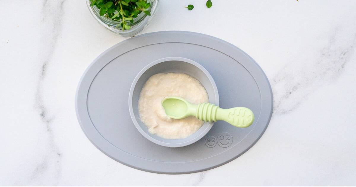 Spoon with vanilla pudding, baby food in hand on a white backgro