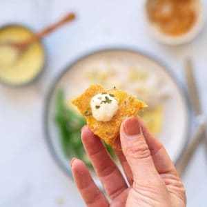 A chicken skin chip toped with a dollop of aioli being held up to the camera.