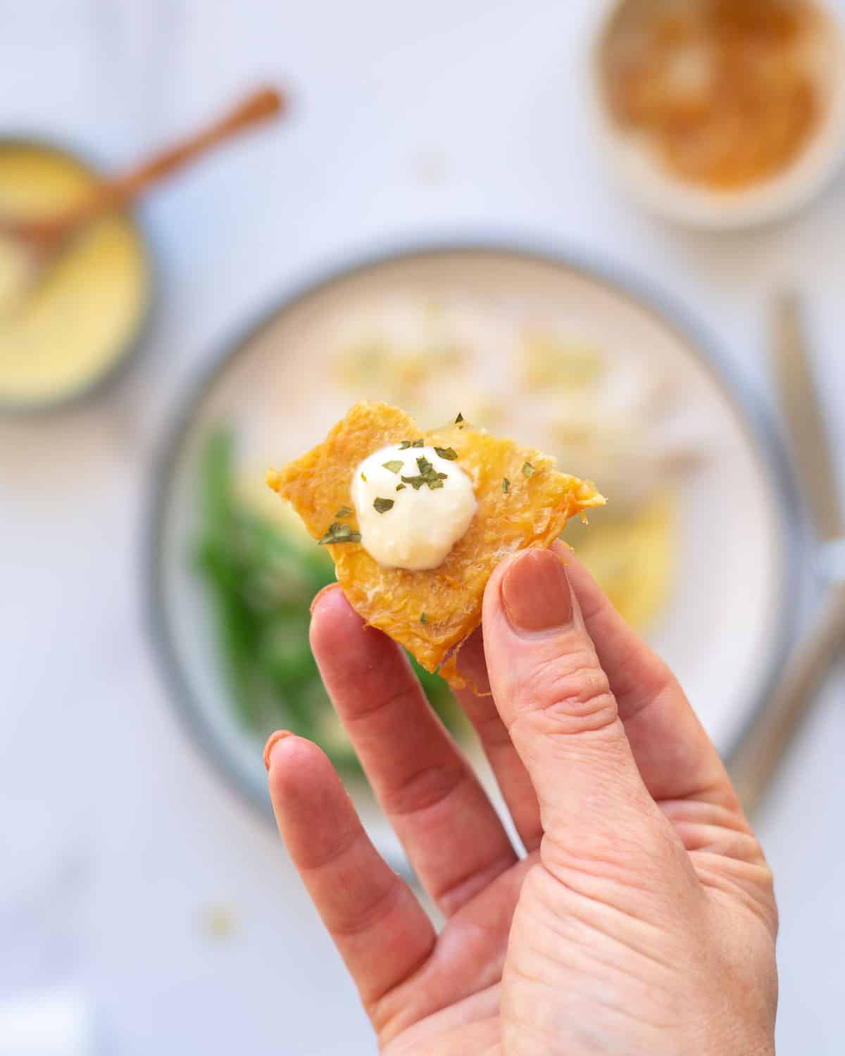 A chicken skin chip toped with a dollop of aioli being held up to the camera. 