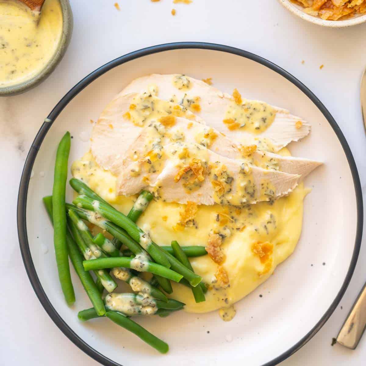 Slices of chicken breast on mashed potatoes with green beans and a yellow sauce. 