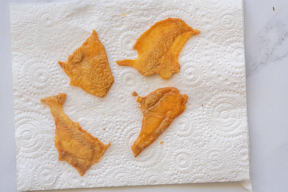 Golden brown chicken skins laid out on a piece of paper towel. 