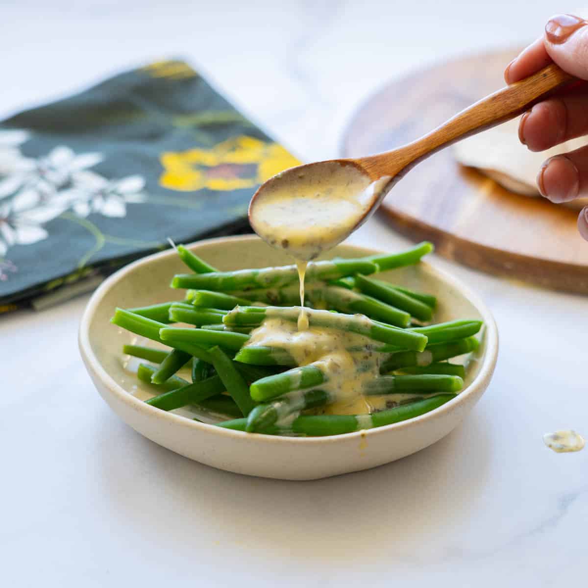 A yellow sauce being drizzled over green beans from a wooden spoon.