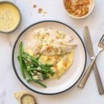 Slices of chicken breast on mashed potatoes with green beans and a yellow sauce.
