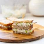 Shredded chicken sandwiches stacked on a wooden board and held together with a bamboo toothpick.