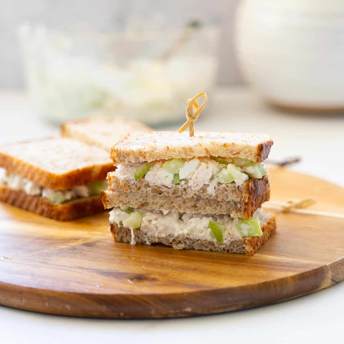 Shredded chicken sandwiches stacked on a wooden board and held together with a bamboo toothpick.