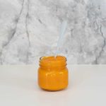 A jar filled with orange puree in front of a marble splash back.