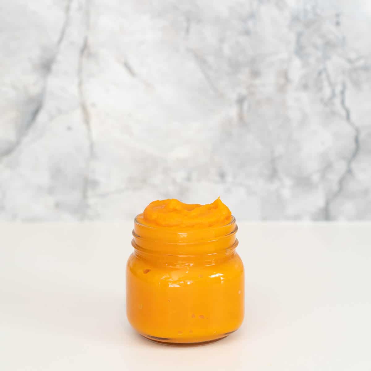 A small glass jar filled with orange baby puree