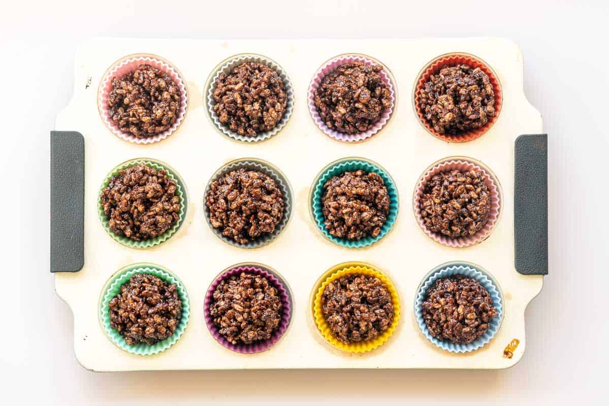 Chocolate crackle mix in 12 multi coloured cupcake liners in a muffin tin.