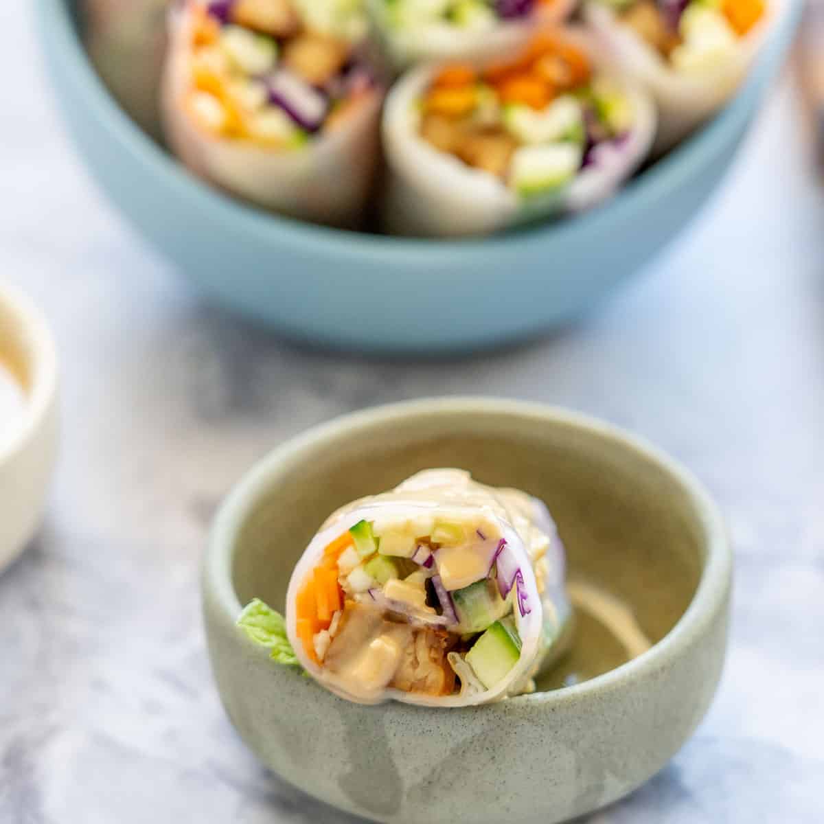 A vietnamese rice paper roll filled with colourful vegetables resting in a small ceramic bowl.