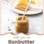A glass jar of seed butter on a marble bench top with a slice of toast and sliced banana in the background, with text overlay for pinterest.