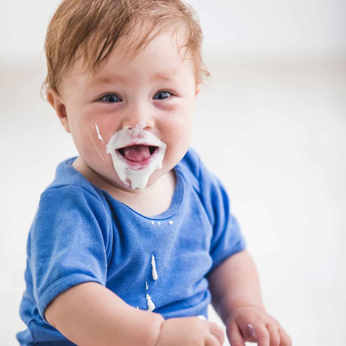 A baby with yogurt around their mouth in a blue baby outfit. 