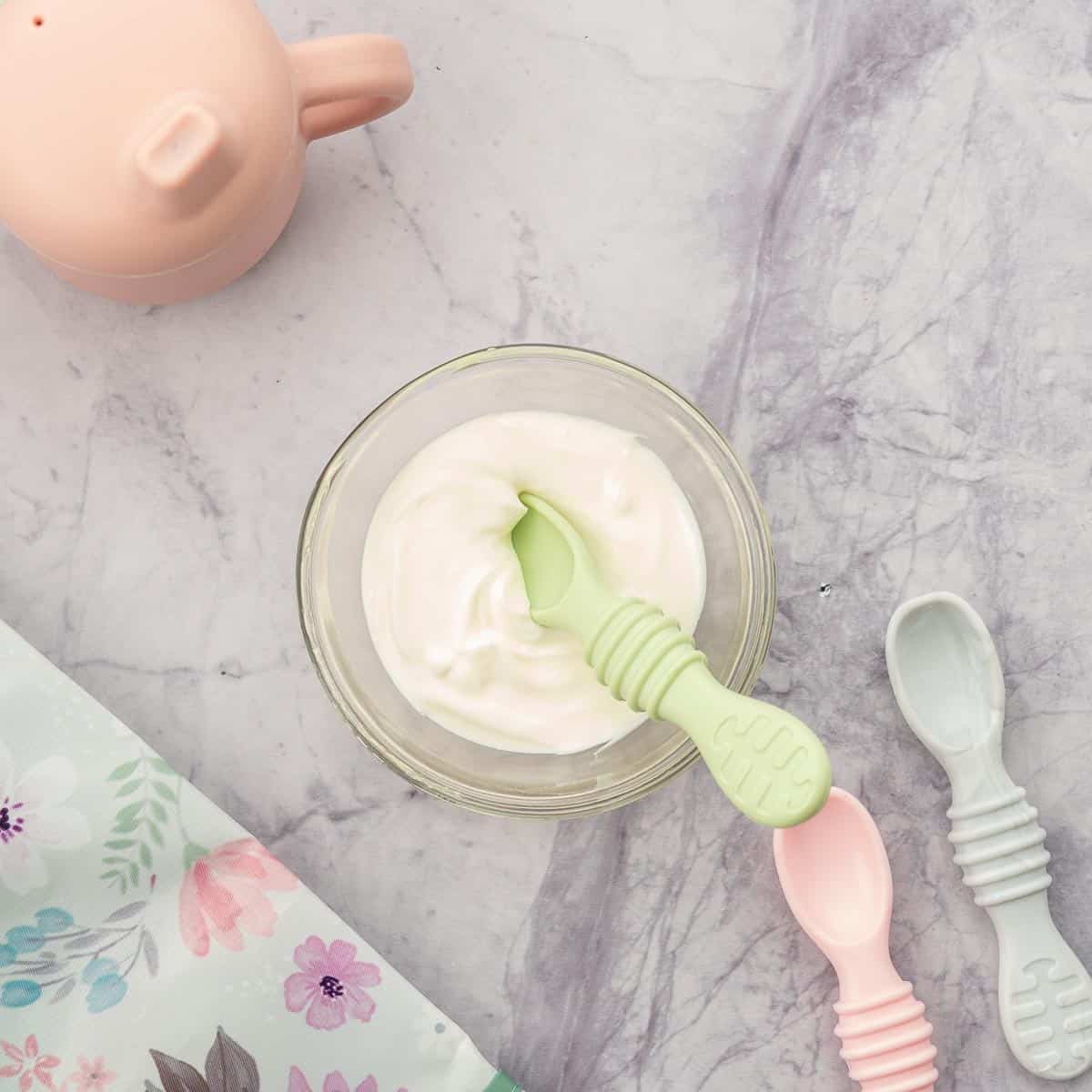 A small bowl of plain yogurt with a baby spoon next to a sippy cup.