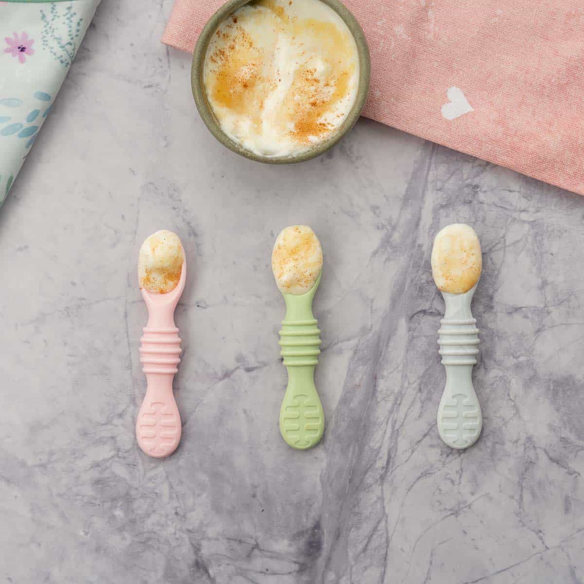 Three short handled baby spoons loaded with yogurt.