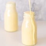 Banana milk being poured into a small glass bottle until it overflows.