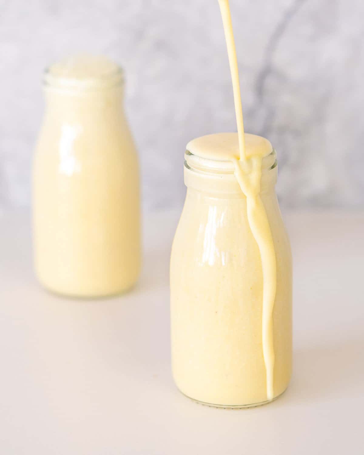 Banana milk being poured into a small glass bottle until it overflows. 