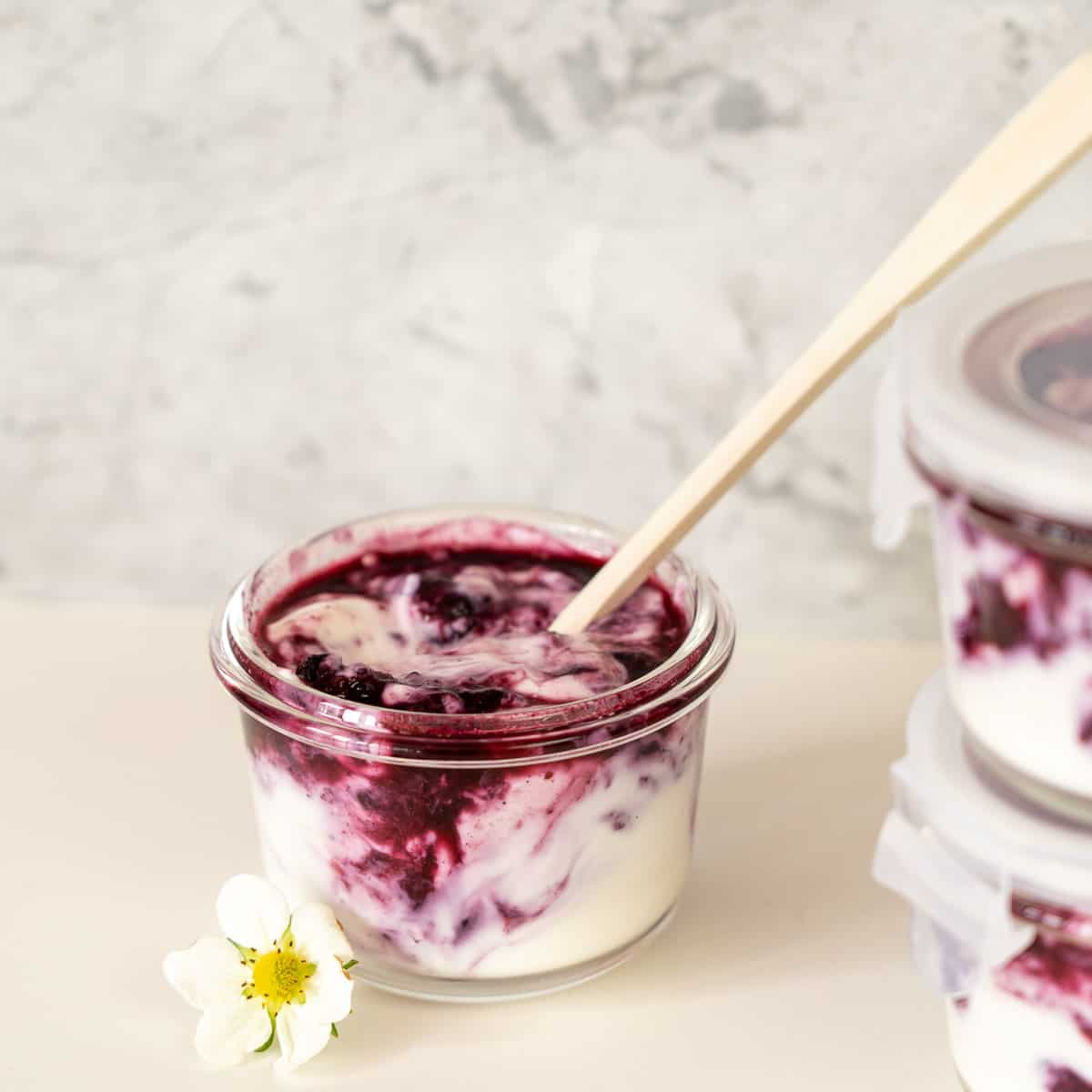 A glas jar of swirled blueberries and yogurt with a long handled bamboo spoon.