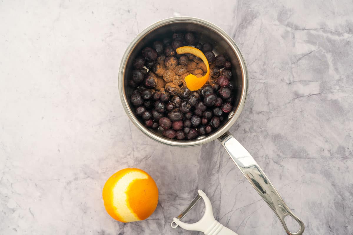 Blueberries and cinnamon in a pot with a strip of orange peel. 