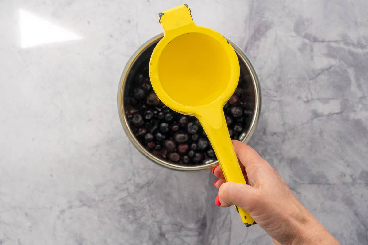 A citrus squeezer being held above a pot of blueberries.