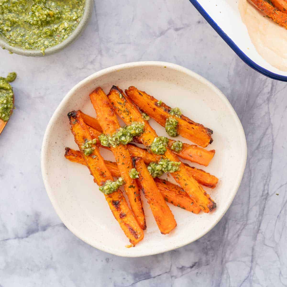 Carrot fries on a ceramic side plate drizzled with pesto sauce.