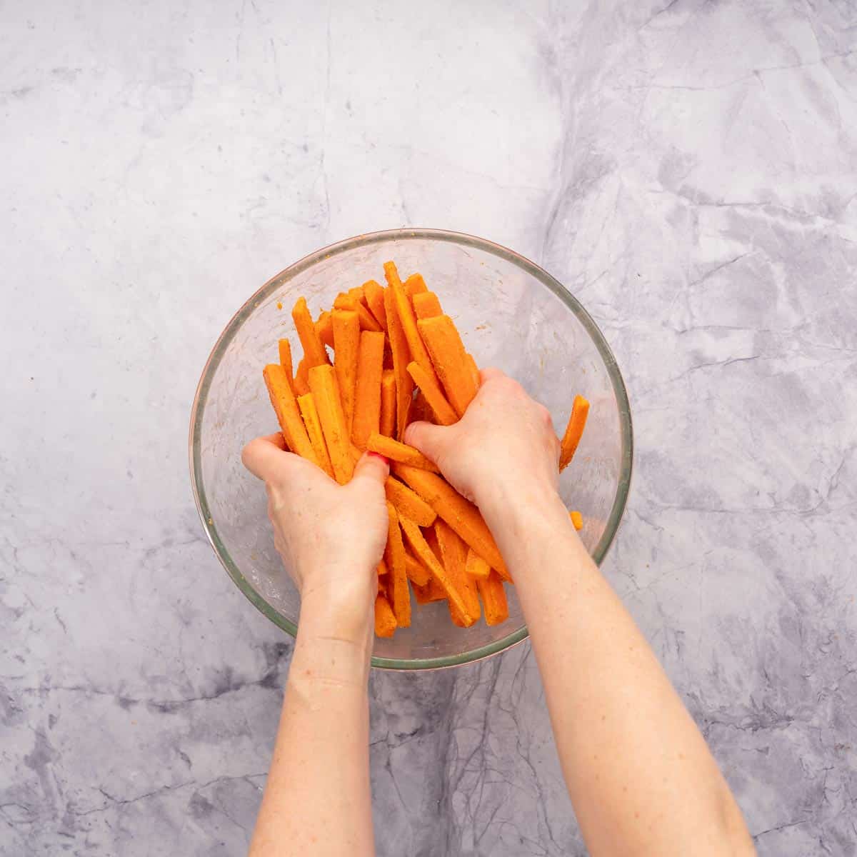 Hand in a mixing bowl rubbing paste onto carrot sticks. 