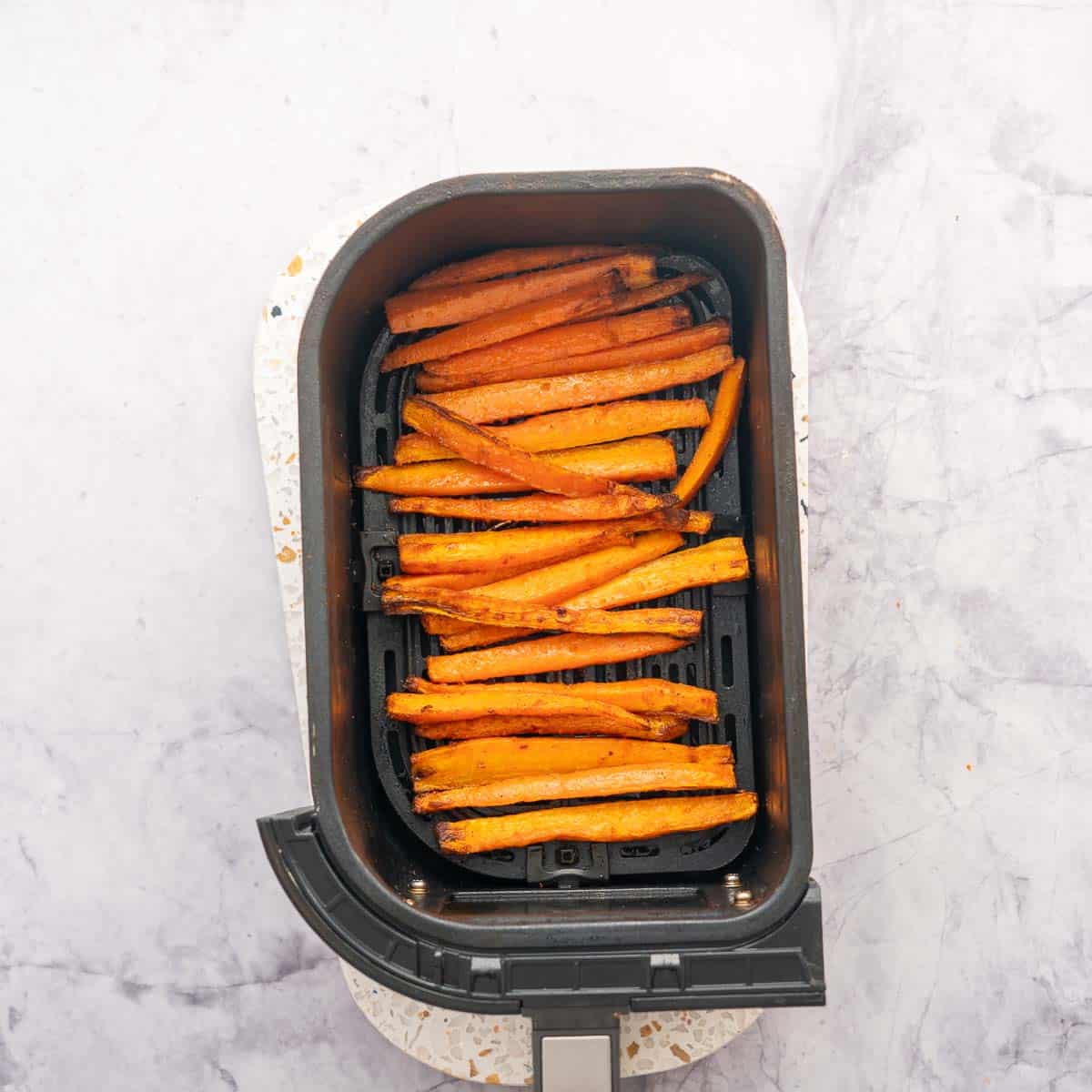 Cooked and blackened carrot fries in an air fryer basket. 