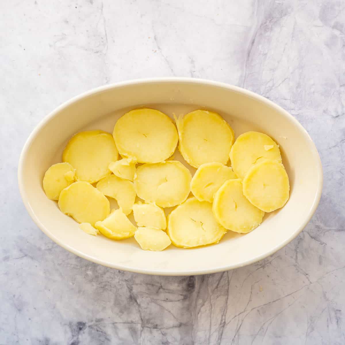 Slices of cooked potato in the bottom of an oval baking dish.