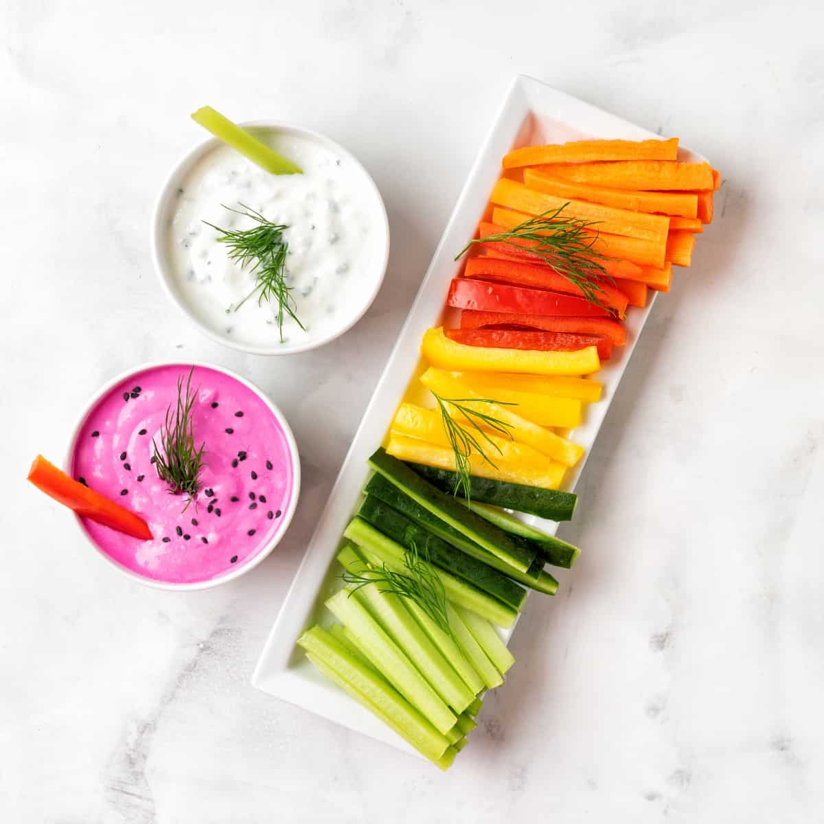 A bowl of yogurt dip with a platter of vegetable batons.