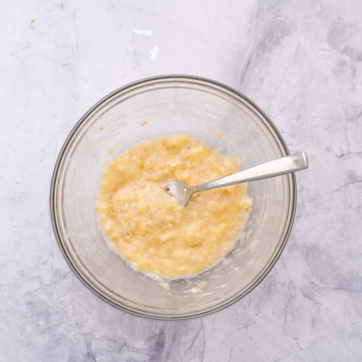 a mixing bowl of mashed banana with a fork