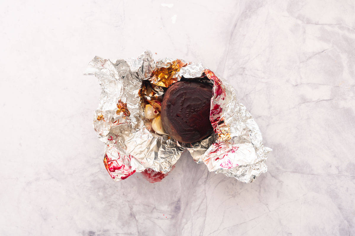 Cooked beetroot and garlic unwrapped in a sheet of tinfoil sitting on the bench. 